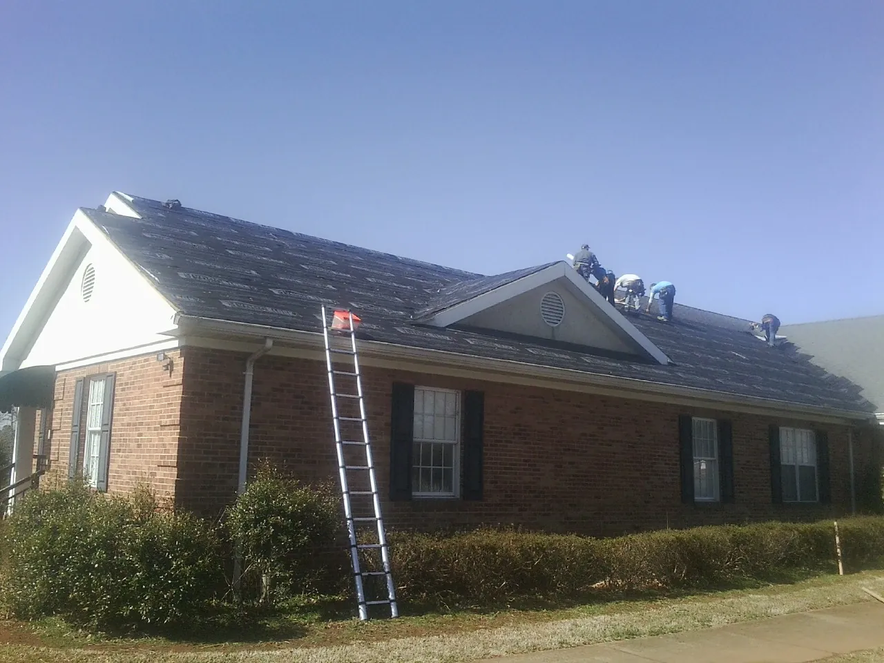 Crew tearing shingles off a brick ranch roof with a ladder set — Metal Roof Repair work by our crew in Rockford
