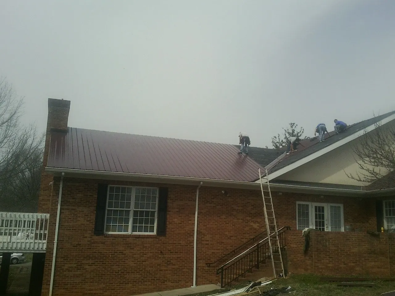 Crew setting red metal roofing panels on a brick home in Rockford
